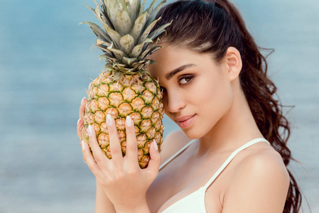 穿白色比基尼的女孩的肖像在海边捧着甜菠萝