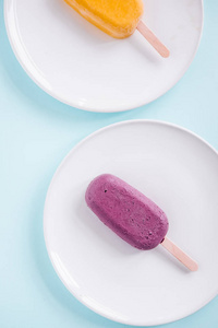 原生素蓝莓和芒果冰棒从上面的白色盘子。柔和的蓝色背景。简约食品摄影, 博客理念。Copyspace, 垂直