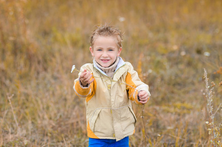 可爱的小男孩穿着黄色夹克在秋天的草地上散步
