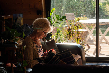 一个老妇人读一本书坐在沙发上。