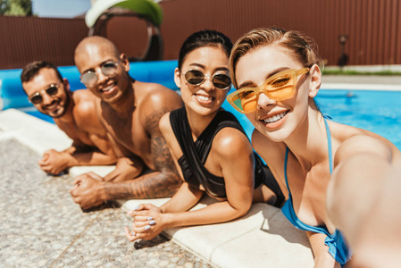 年轻的微笑多文化的人在泳装和太阳镜在游泳池摆姿势