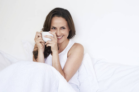 微笑的妇女与早晨咖啡在床上