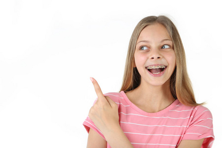 年轻的微笑的女孩与牙齿括号指向白色背景的手指
