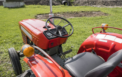 一辆小型小型红色拖拉机站在农场草坪上的绿草上, 等待工作开始。
