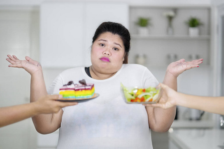 困惑超重的女人不知道什么选择彩虹蛋糕和沙拉