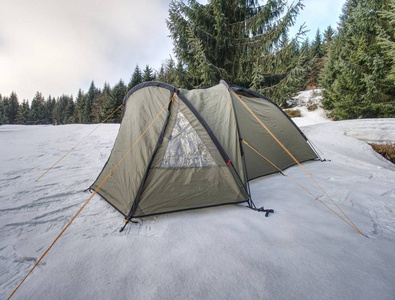 风景与徒步帐篷在雪之下。清晨阳光下的绿色帐篷与冰冻湖泊表面