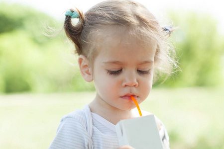 阳光明媚的画像一个小孩子喝从稻草 juiceon 模糊的夏季背景