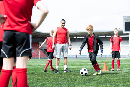 少年足球队的全长肖像练习, 重点放在红头发少年男孩带领球与教练看他, 复制空间