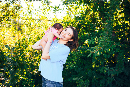 年轻美丽的母亲与深色的头发抱着她的新生女婴在粉红色的 t恤爱的家庭吻女儿微笑着在公园绿树
