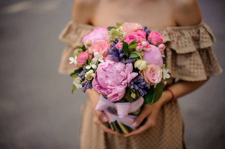 穿着米色连衣裙的女人手里拿着一束浪漫的玫瑰花和牡丹花。