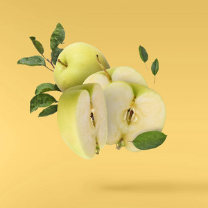 飞在空气绿色新鲜整体和切开苹果并且叶子在黄色背景, 食物悬浮概念, 优质