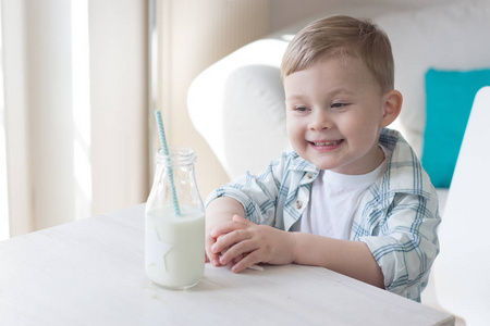 一个可爱的小男孩是吃糖果和喝牛奶。健康。快乐的孩子。早餐。一个小男孩正坐在桌旁