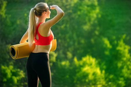 在红色的顶部和黑色裤子的年轻金发女郎认为自然界中的喷泉垫。一个女人准备体操