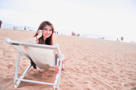 亚洲小姐在椅子在海滩上打手机
