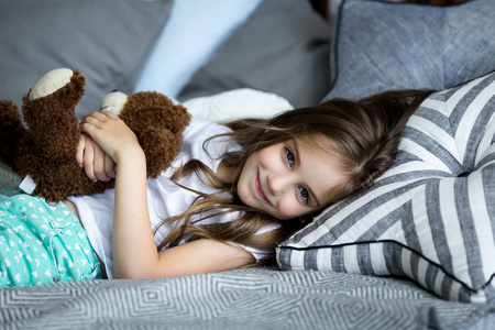 可爱的小女孩正在玩一只玩具熊在床上