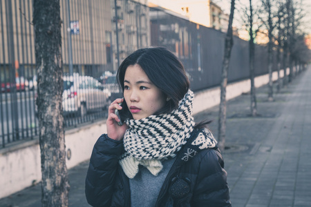 年轻漂亮的中国女孩谈电话在城市的街道