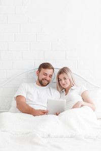 年轻人和幸福的夫妇与平板电脑在床上