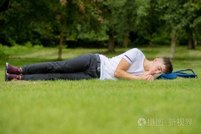 十几岁的男孩躺在草地上在一个夏天一天照片-正版商用