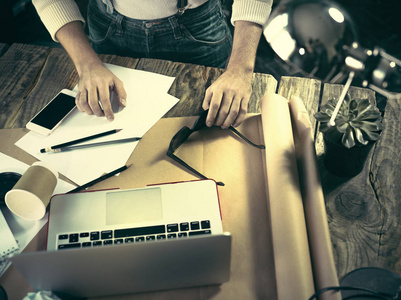 复古时髦木制桌面顶视图，使用一台笔记本电脑和拿着铅笔的男性手