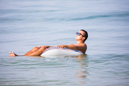 太阳镜，一杯啤酒漂浮在海水中的橡胶环上的年轻人