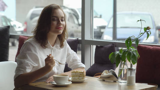 年轻美丽的女子享有香的咖啡和甜甜的蛋糕，坐在咖啡屋。休息休息期间的女商人