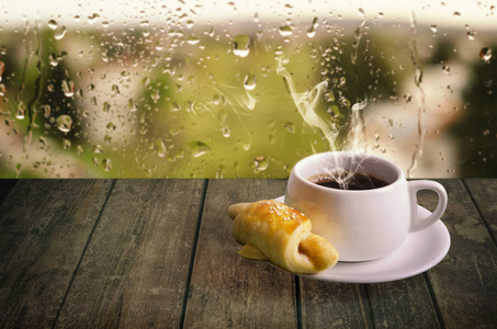 在雨天窗口背景上杯热气腾腾的咖啡