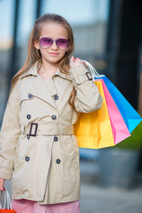 可爱的小女孩，用购物袋户外的画像。欧洲城市户外时尚蹒跚学步的孩子