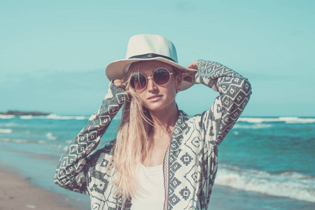 白帽子和太阳镜热带的巴厘岛在阳光明媚的日子走在白色的沙滩上一个年轻女子的画像。海洋成本