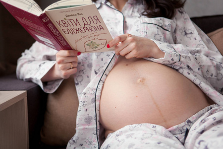 怀孕的女人坐在沙发上，阅读本书的特写