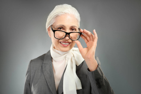 美丽优雅的老年妇女，戴着眼镜在灰色的背景上