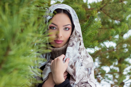 年轻漂亮的女人，与冬季的森林附近杉木树，雪落在她头上的围巾