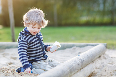 可爱的蹒跚学步的男孩在户外操场上玩沙子