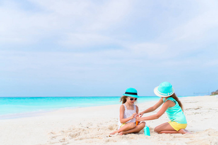 两个关爱女孩照顾彼此在白色的沙滩上。保护免受紫外线辐射的概念