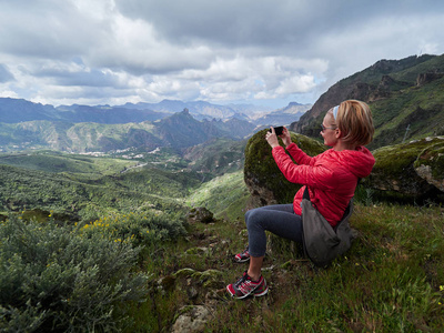 女游客坐在悬崖边，拍照片
