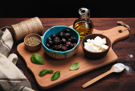 产品的地中海菜肴。中蓝 橄榄油和一碗乳酪在黑暗的木制背景上的棕色砧板上的干的橄榄。黑色背景上的文字的地方
