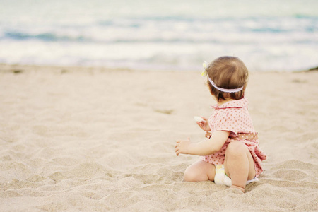 可爱的小宝贝女孩与一个穿着波尔卡点坐在海边的沙，望向大海