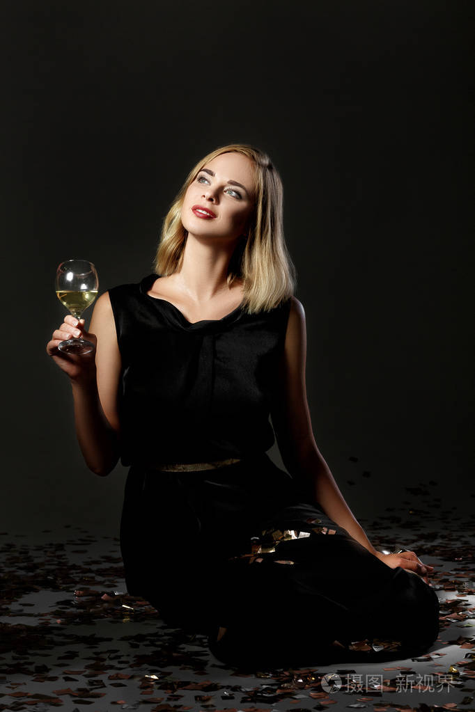 美丽的金发女人在黑色背景上的白色葡萄酒杯
