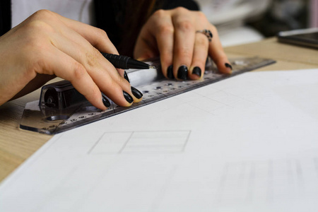 年轻女子建筑师画的计划，设计，图形的几何形状由铅笔在大张纸放在办公桌上。作物图像