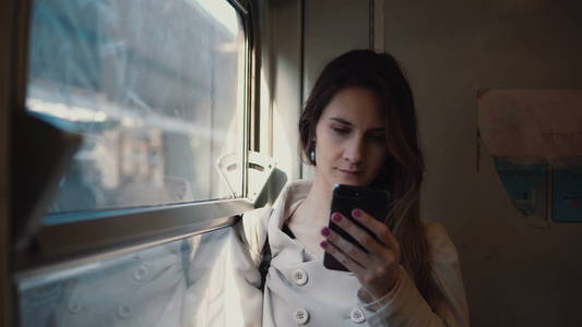女孩站在火车和使用智能手机的画像。年轻女子发短信 sms 和浏览互联网