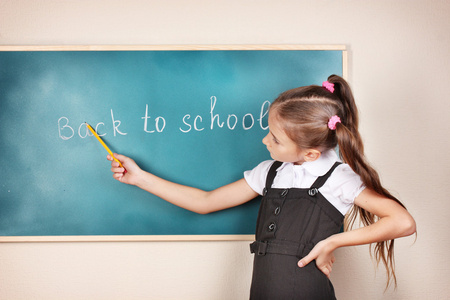 漂亮的小女孩站在教室里的黑板旁边
