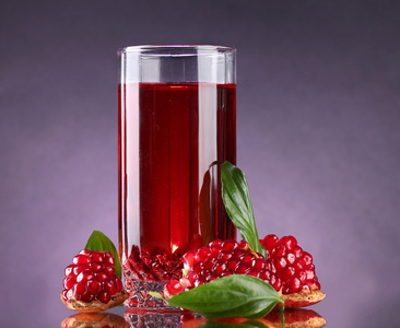 成熟的 pomergranate 和杯果汁上紫色背景