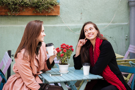 两个微笑的女人喝咖啡和谈话在户外咖啡馆