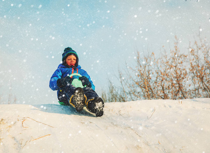 孩子们冬天好玩滑动在雪地里的小男孩