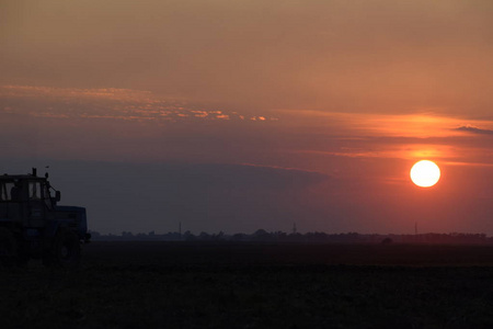 拖拉机在夕阳下犁地.日落背景上的拖拉机剪影。