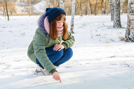 一个年轻的女孩写在雪地中冬季公园手指上