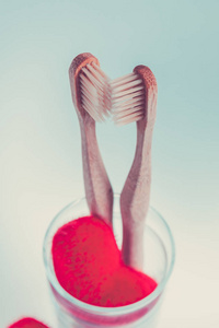 两个米色的牙科笔刷在玻璃杯子用红色蓝色白色背景上的心。孤立。健美的照片。爱。情人节