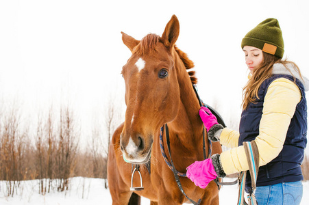在冬天的衣服的女人正骑在一匹马，背景为白色的雪