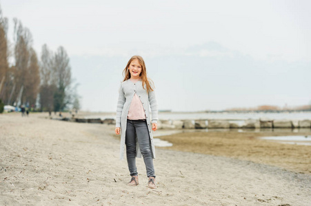 可爱的小女孩的 89 岁玩在湖边，穿着灰色的裤子和长羊毛衫