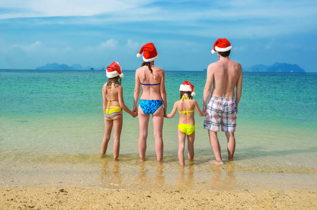 在圣诞和新年假期，快乐的家长和孩子在圣诞老人的帽子上的家庭度假海滩上玩的旅游带孩子