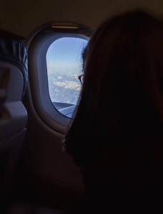 好奇的单身女人戴着眼镜乘飞机旅行，从窗户上方欣赏群山
